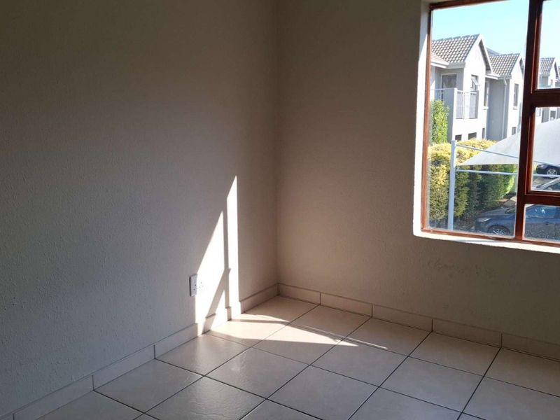 A bright, empty bedroom featuring neutral tiled flooring and a large window with views of the complex parking area.