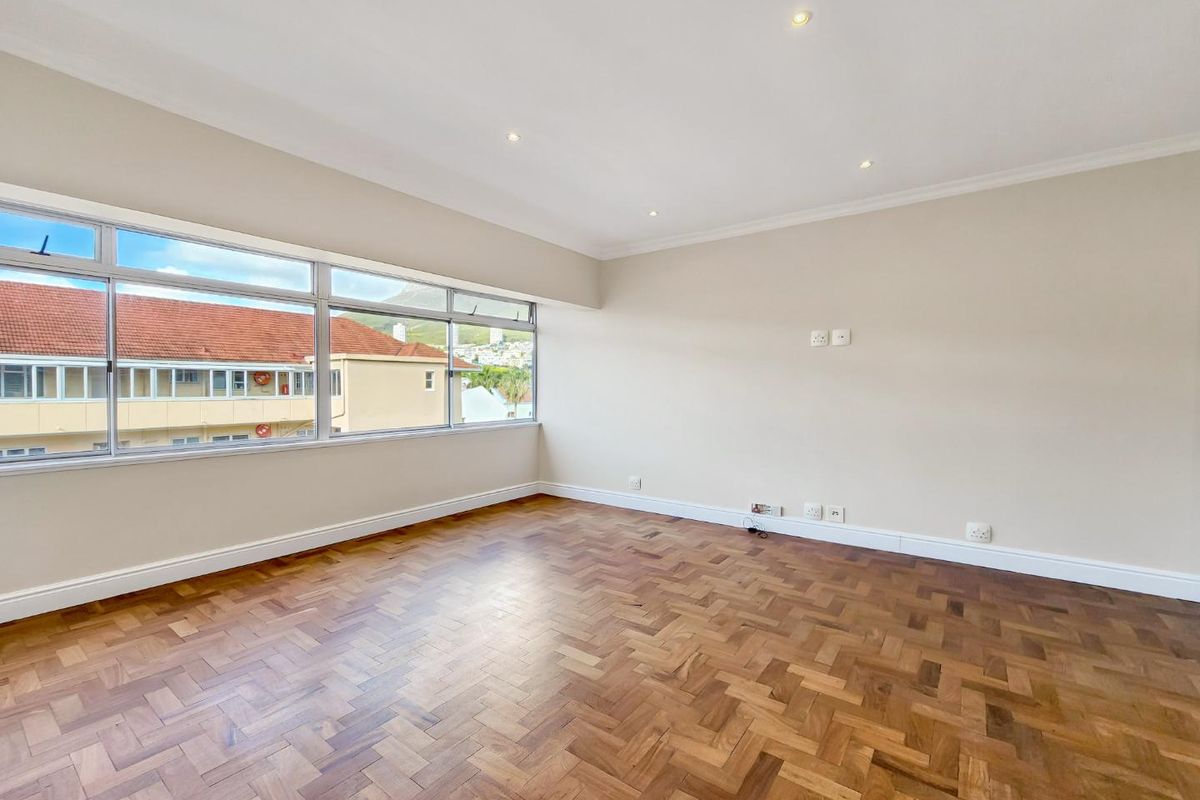 A bright and spacious living area featuring classic herringbone parquet flooring, recessed lighting, and large windows offering natural light and neighborhood views.