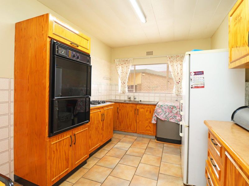 A functional kitchen featuring traditional wooden cabinetry, a double wall oven, gas hob, and tiled flooring with a practical layout.