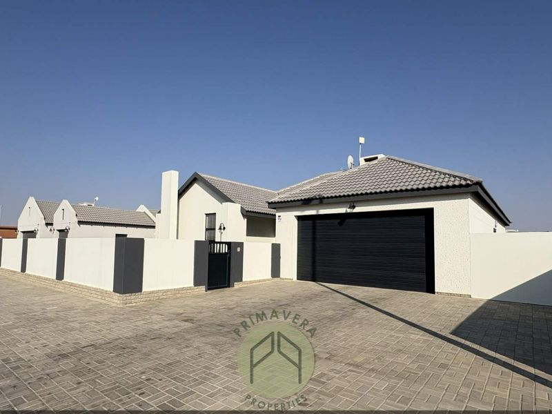 Modern residential exterior featuring a paved driveway, secure perimeter wall, and a double garage with a sleek black door.