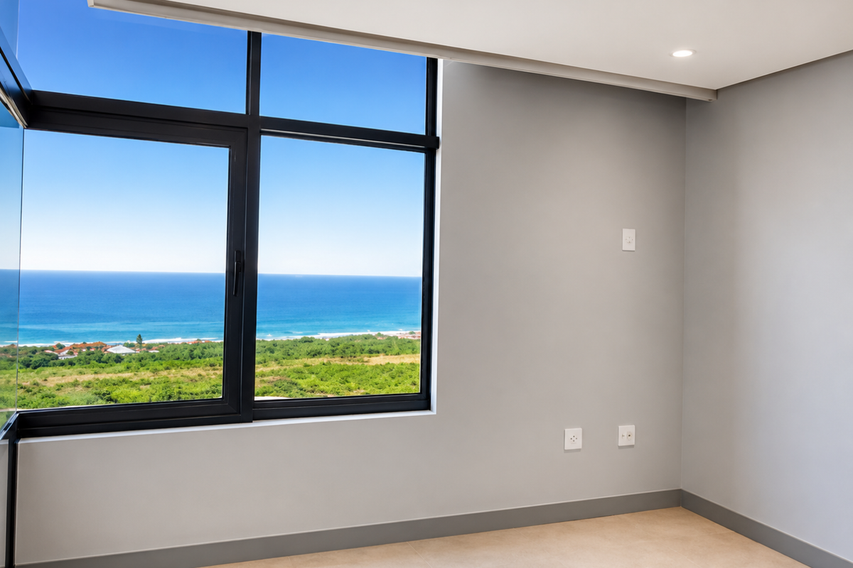 A bright, empty bedroom featuring large aluminium-framed windows with expansive ocean and coastal views, neutral wall finishes, and modern tiled flooring.