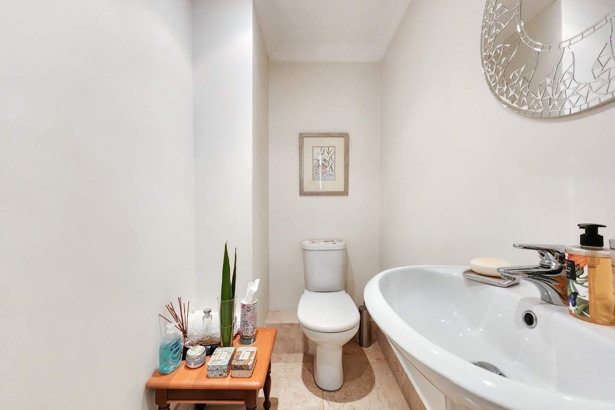 A compact guest bathroom featuring a pedestal basin with chrome mixer tap, a standard toilet, and neutral stone floor tiling.