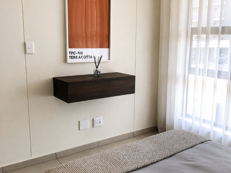 A well-maintained bedroom featuring neutral wall tones, tiled flooring, a floating wall-mounted shelf, and large windows with sheer curtains.