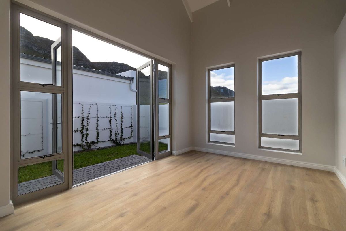 A bright, modern living area featuring light wood-look flooring, high ceilings, and large glass doors opening onto a private garden patio.