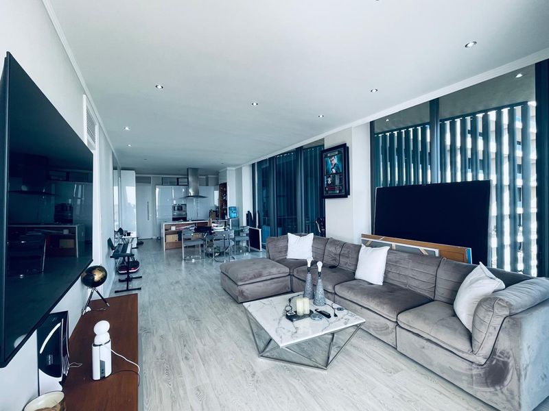 Spacious open-plan living and dining area featuring modern laminate flooring, recessed lighting, and a sleek kitchen with integrated appliances and floor-to-ceiling windows.