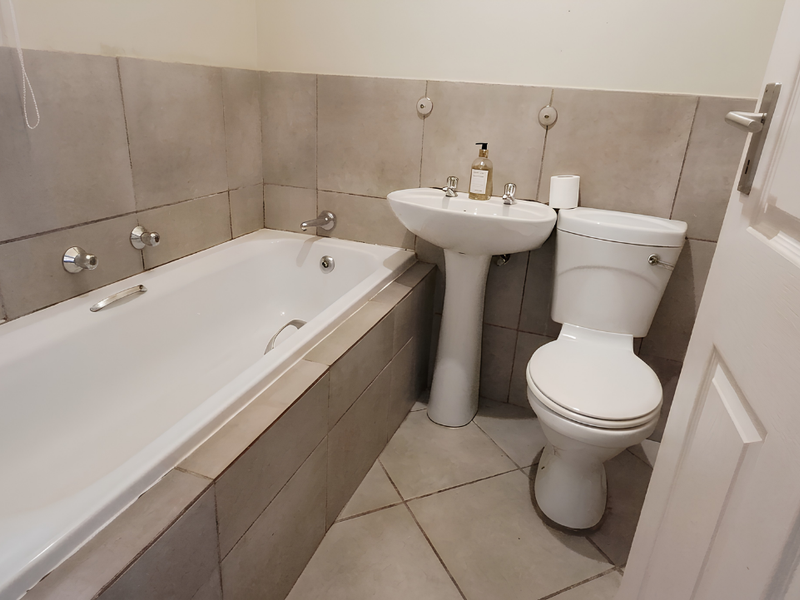 A functional bathroom featuring a built-in bathtub, pedestal basin, and toilet with neutral ceramic wall and floor tiling.
