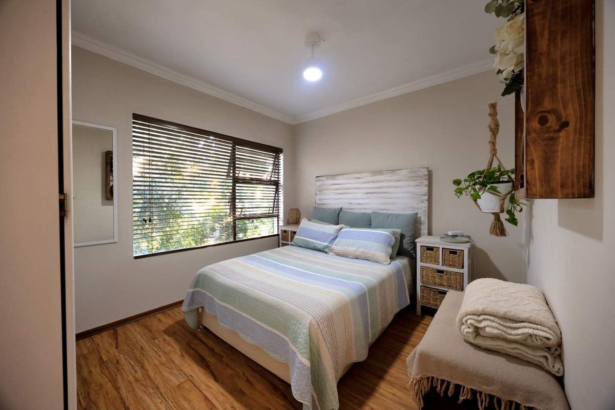 A well-maintained bedroom featuring warm-toned laminate flooring, neutral wall finishes, and large windows fitted with venetian blinds for natural light control.