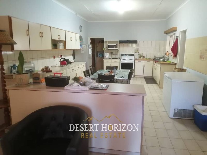 A functional kitchen featuring built-in cabinetry, a tiled backsplash, a stove with an extractor fan, and a breakfast counter overlooking the living area.