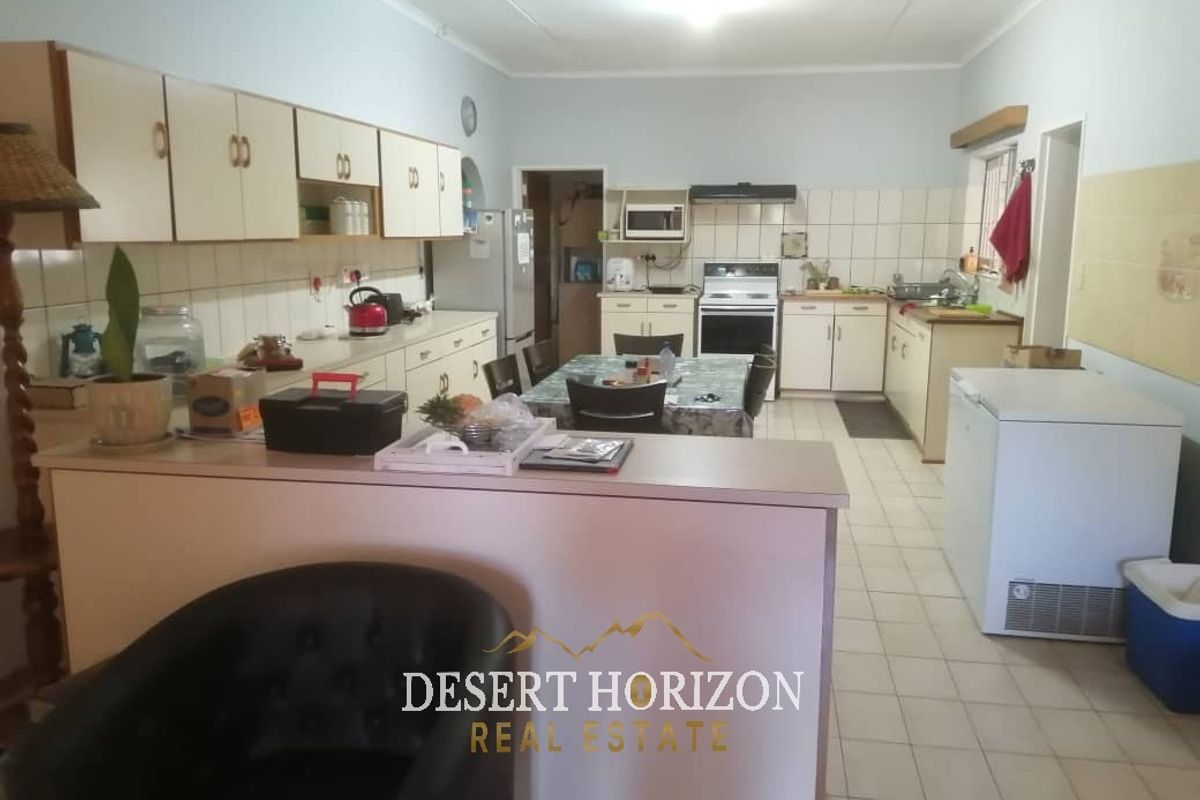 A functional kitchen featuring built-in cabinetry, a tiled backsplash, a stove with an extractor fan, and a breakfast counter overlooking the living area.