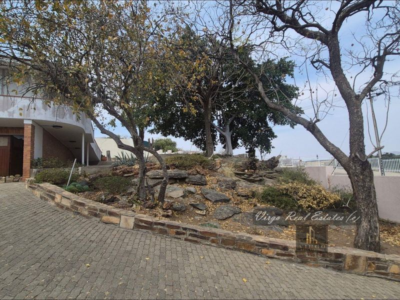 Front exterior view featuring a paved driveway, stone retaining wall, and established rock garden leading to the main building entrance.