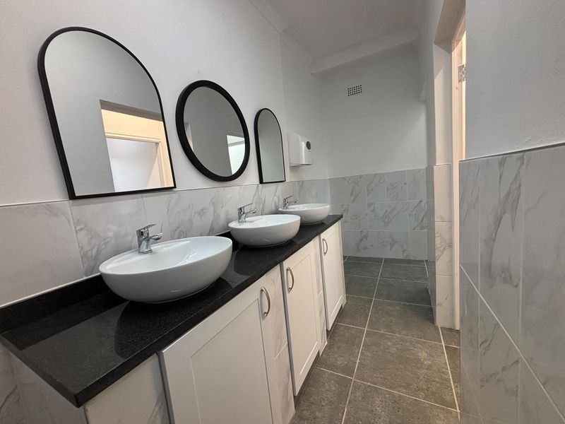 Modern office bathroom featuring a triple vanity with vessel sinks, stone countertop, and contemporary marble-look wall tiling.