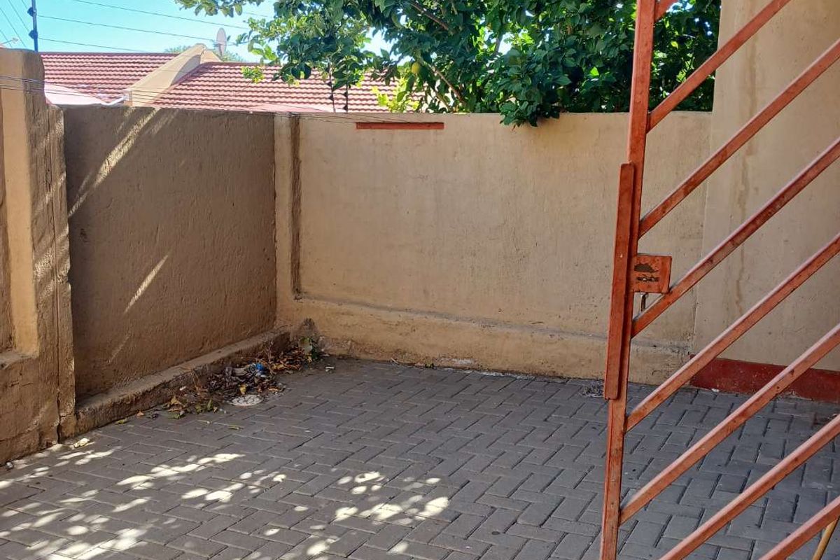 A paved outdoor courtyard area featuring a metal security gate and perimeter boundary wall, requiring maintenance and cleaning.