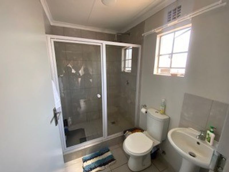 A functional bathroom featuring a glass-enclosed shower, pedestal basin, and toilet with neutral tiled finishes.