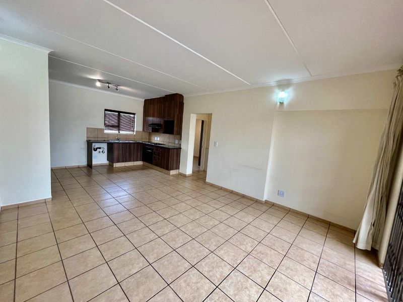 An open-plan living and kitchen area featuring tiled flooring, built-in cabinetry, and integrated kitchen appliances in a clean, vacant space.