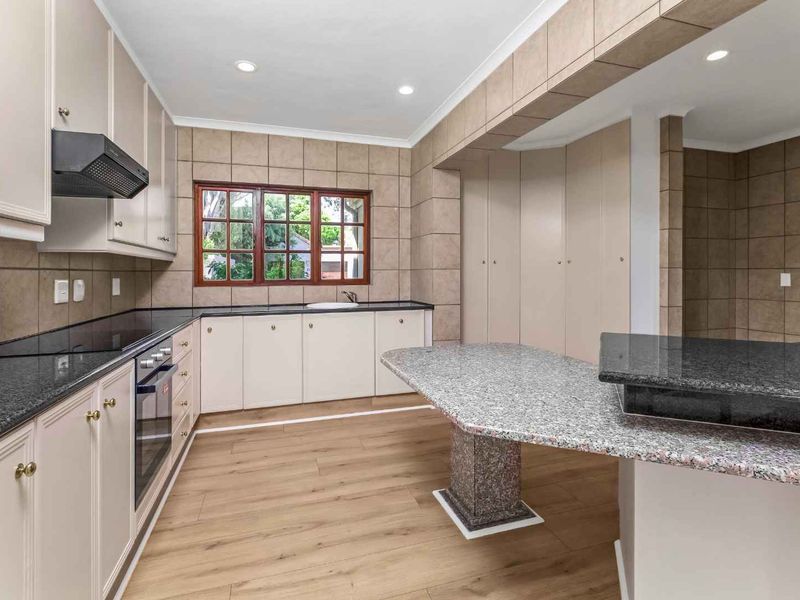 A spacious, well-lit kitchen featuring granite countertops, built-in cabinetry, an integrated oven, and modern laminate flooring.