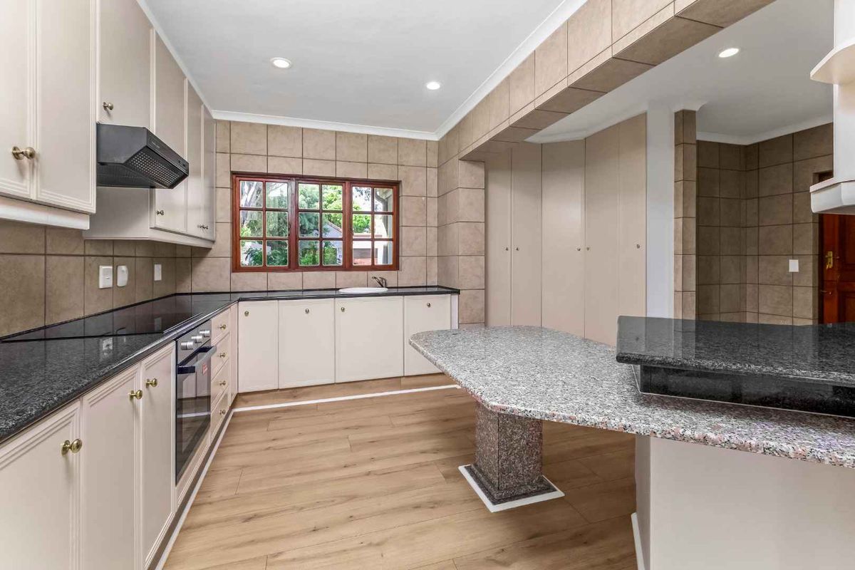 A spacious, well-lit kitchen featuring granite countertops, built-in cabinetry, an integrated oven, and modern laminate flooring.
