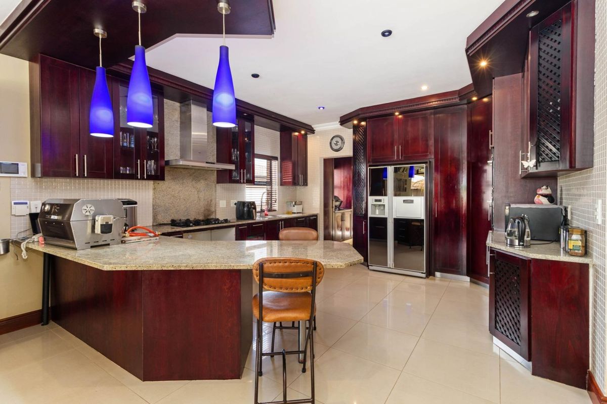 Spacious kitchen featuring dark wood cabinetry, granite countertops, a breakfast bar, stainless steel extractor fan, and tiled flooring.