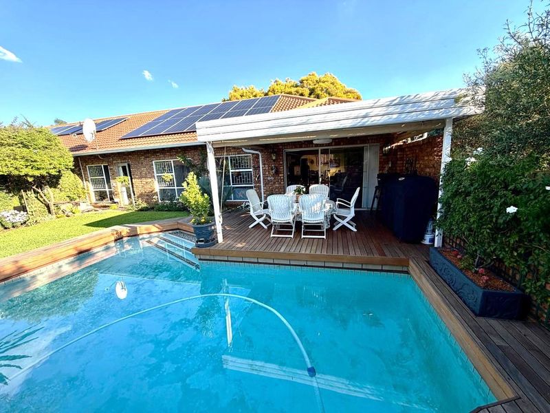 A well-maintained outdoor area featuring a swimming pool, timber decking, and a covered patio attached to a brick townhouse with solar panels.