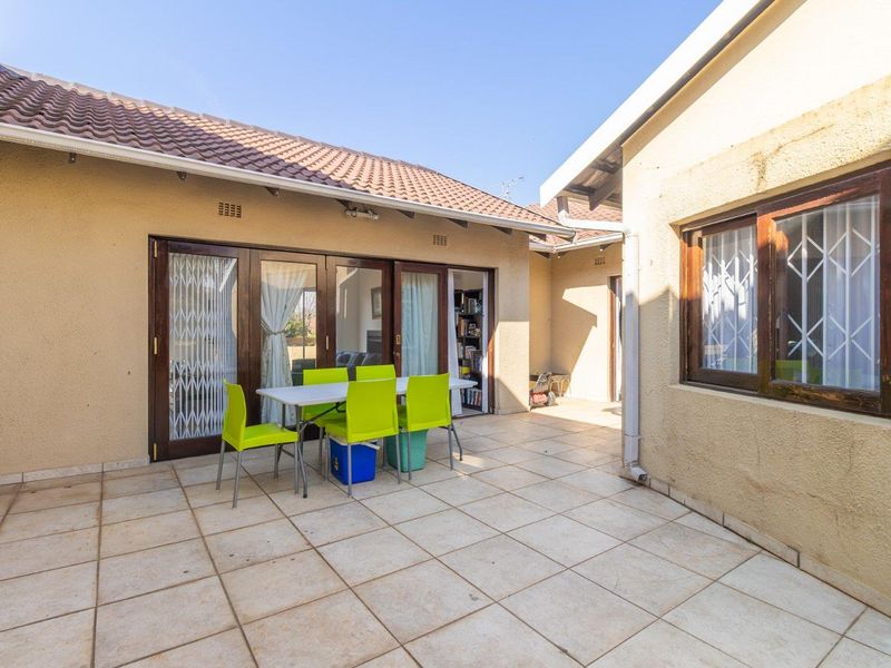 A paved outdoor patio area featuring sliding glass doors with security gates, providing seamless access to the interior living space.