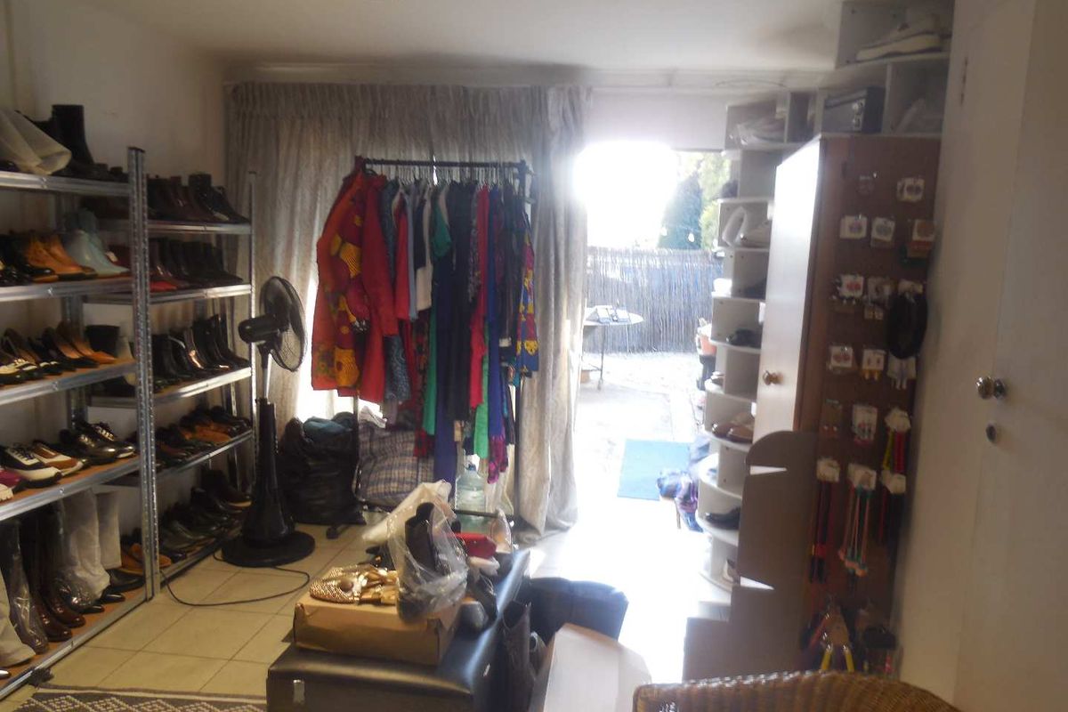 An office space currently utilized for storage, featuring tiled flooring, recessed lighting, and built-in shelving units with direct access to an outdoor area.