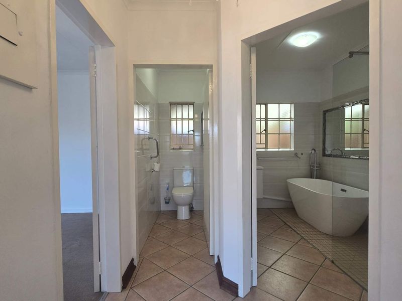 A hallway view leading into a separate toilet and a bathroom featuring a modern freestanding bathtub and tiled flooring.