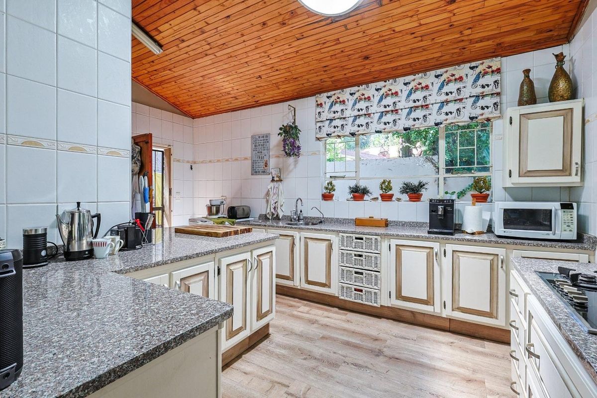 A functional kitchen featuring granite countertops, built-in cabinetry, a timber-clad ceiling, and a large window providing natural light.