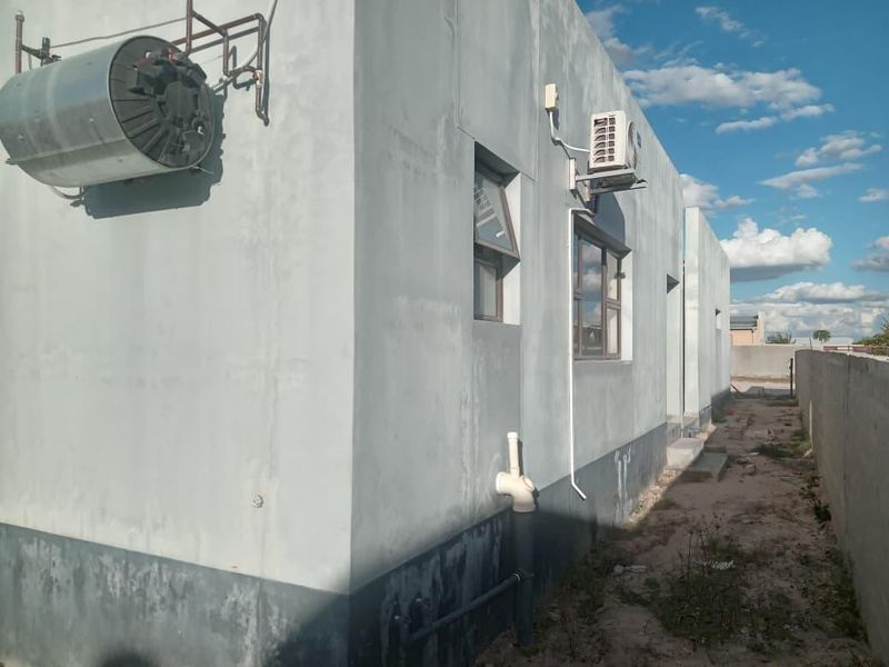 Rear exterior view of the property showing exposed utility infrastructure, including an external geyser, air conditioning unit, and unfinished wall surfaces.