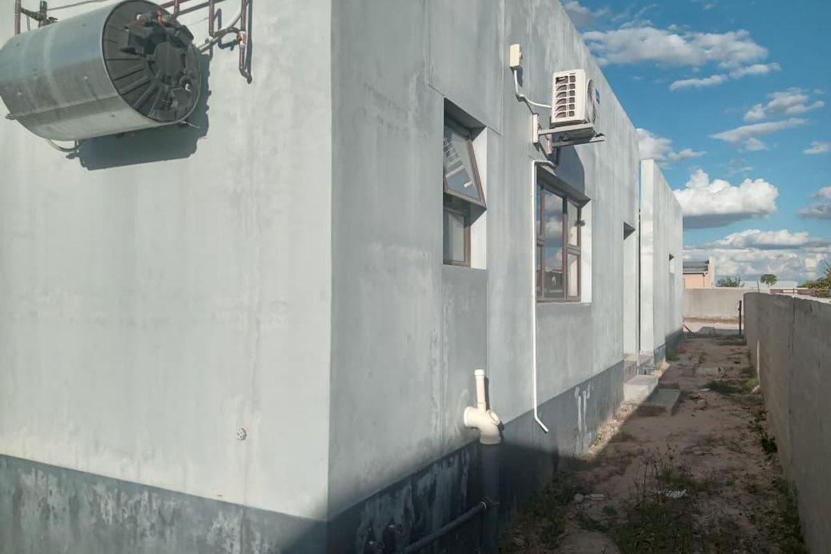 Rear exterior view of the property showing exposed utility infrastructure, including an external geyser, air conditioning unit, and unfinished wall surfaces.