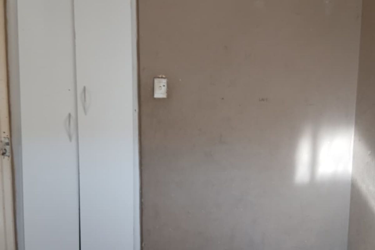 An empty bedroom featuring tiled flooring and a built-in wardrobe, requiring cosmetic updates to the wall finishes.