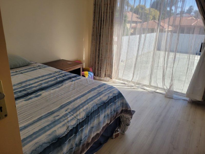 A bedroom featuring light-toned laminate flooring and a large sliding glass door providing access to the exterior.