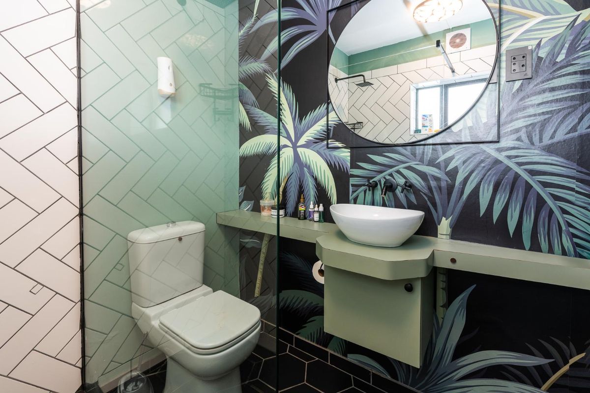 Modern bathroom featuring a wall-mounted vanity with vessel sink, glass shower partition, and decorative palm-print wall tiling.