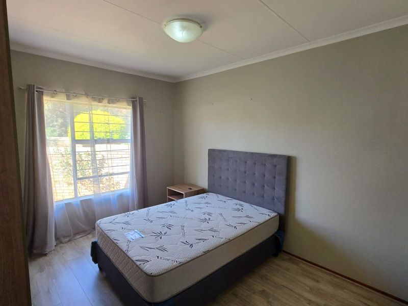 A functional bedroom featuring laminate flooring, neutral wall tones, and a built-in cupboard, offering a clean and simple living space.