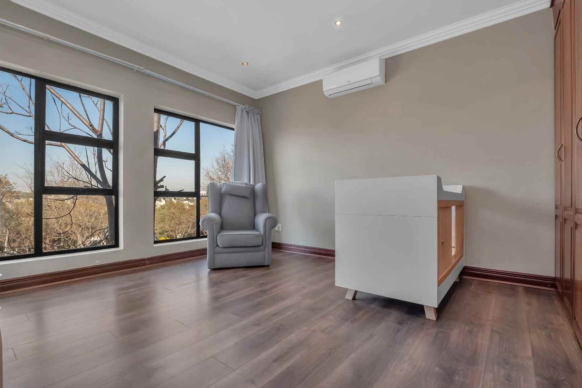 A bright bedroom featuring dark wood-look flooring, large black-framed windows, built-in wooden cabinetry, and a wall-mounted air conditioning unit.