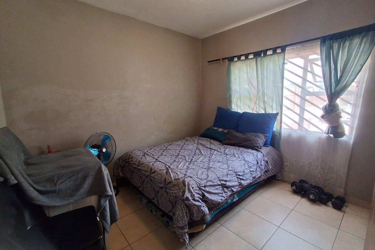 A functional bedroom featuring tiled flooring and a window with security bars, providing a simple and practical living space.