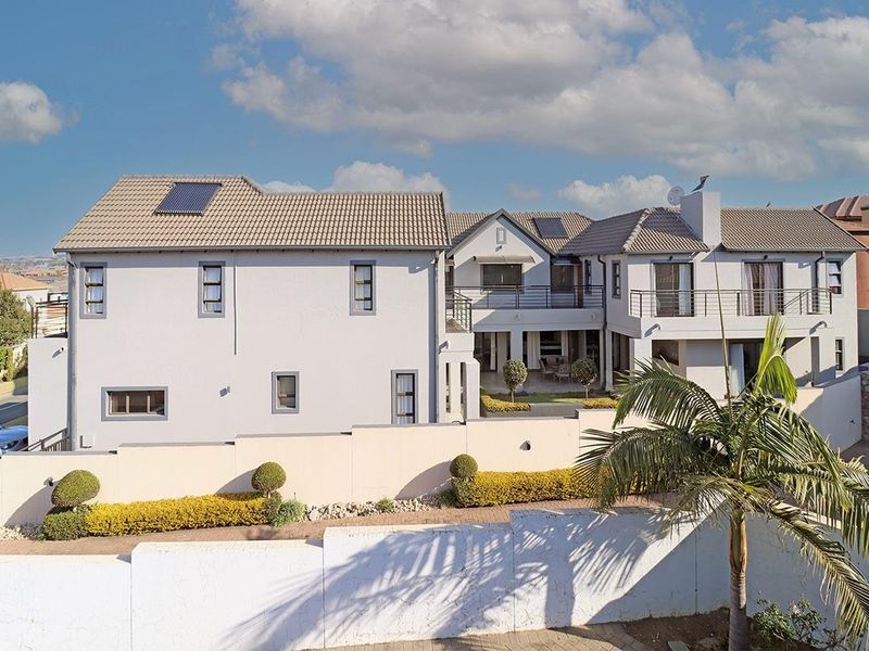Rear view of a multi-story residential property featuring a tiled roof with solar panels, a balcony, and a secure boundary wall.