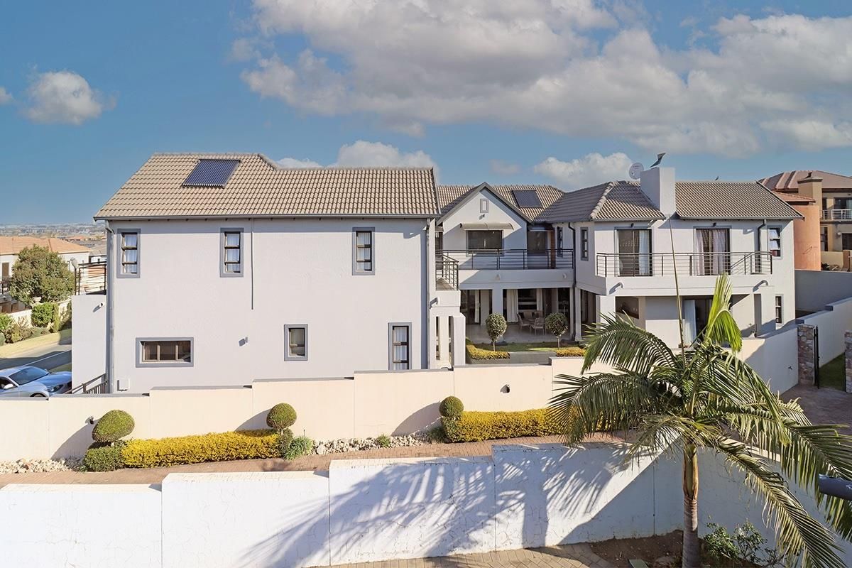 Rear view of a multi-story residential property featuring a tiled roof with solar panels, a balcony, and a secure boundary wall.