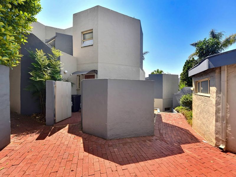 Exterior view of the townhouse entrance featuring brick paved pathways, boundary walls, and modern architectural facade elements.
