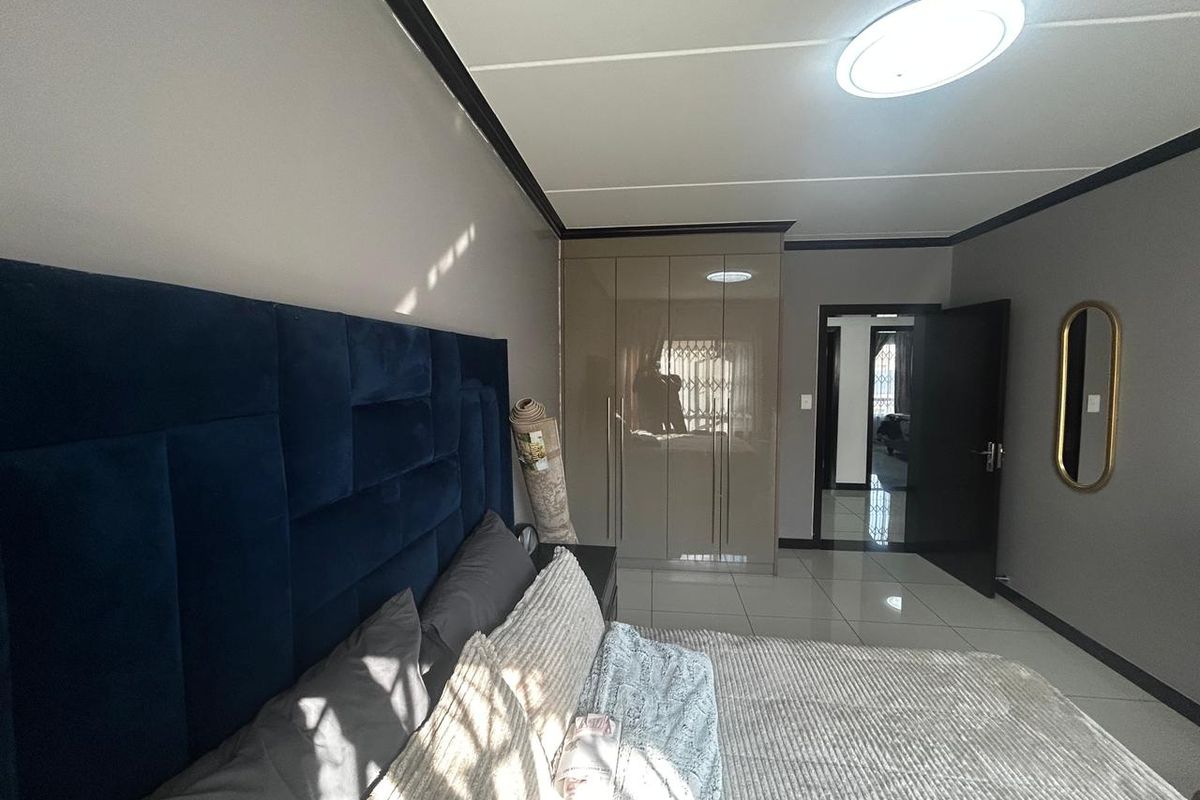 A well-maintained bedroom featuring glossy built-in cupboards, tiled flooring, and modern ceiling lighting, offering a clean and contemporary living space.