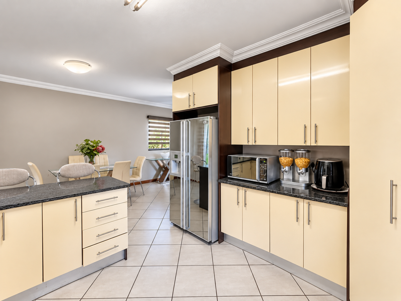 Open plan kitchen and dining area featuring cream cabinetry, granite countertops, tiled flooring, and crown molding, creating a functional and cohesive living space.