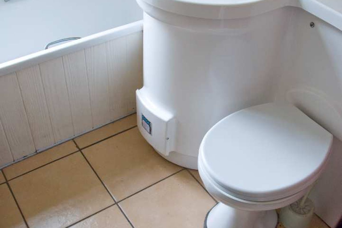 A compact bathroom featuring an integrated vanity sink, toilet, and bathtub with tiled flooring and wall surrounds, presenting a dated aesthetic.