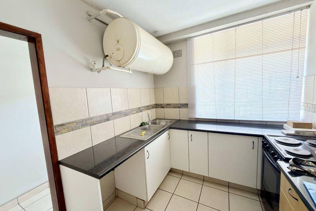 A functional kitchen featuring granite countertops, white cabinetry, a double basin sink, and a wall-mounted geyser, finished with tiled flooring and a tiled backsplash.