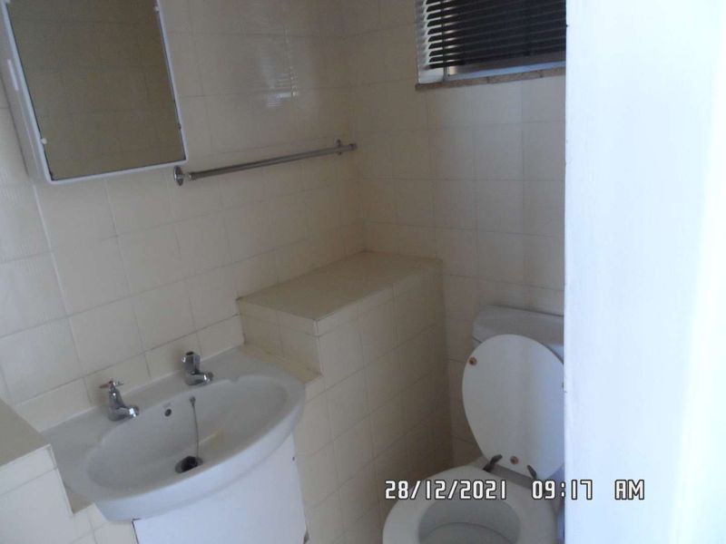 A compact bathroom featuring a pedestal basin, toilet, and tiled walls, requiring cosmetic updates to modernize the space.