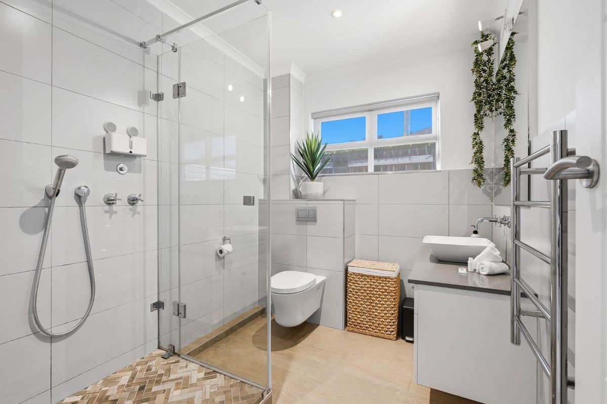 Modern bathroom featuring a glass-enclosed shower, wall-mounted toilet, vessel sink vanity, and a heated towel rail with contemporary tiled finishes.