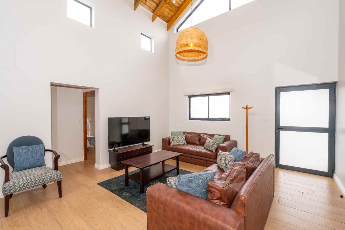Spacious living room featuring high vaulted ceilings with exposed timber beams, large windows, and modern light-toned flooring.