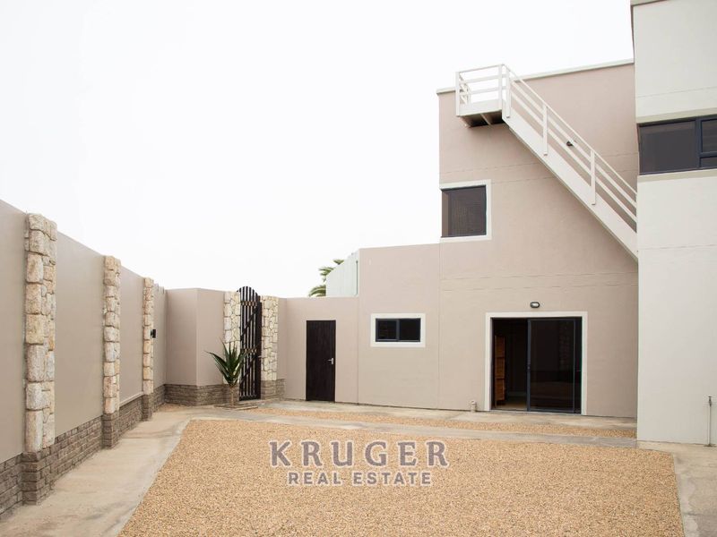 A rear courtyard featuring a gravel surface, stone-accented boundary walls, and an external staircase leading to an upper level.