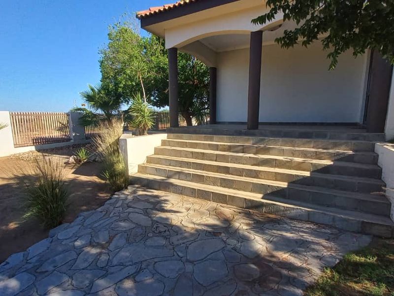 A covered patio area featuring stone paving, concrete steps, and support columns, leading to an outdoor garden space.