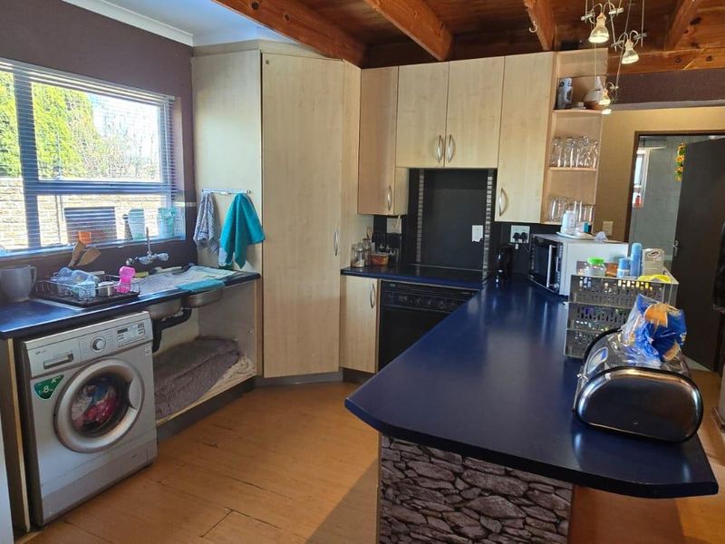 A functional kitchen featuring laminate cabinetry, a breakfast bar, exposed timber ceiling beams, and integrated laundry plumbing.