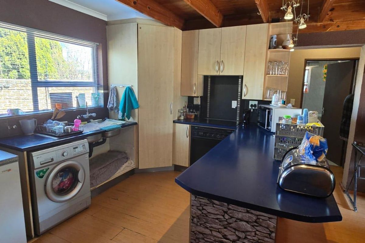 A functional kitchen featuring laminate cabinetry, a breakfast bar, exposed timber ceiling beams, and integrated laundry plumbing.
