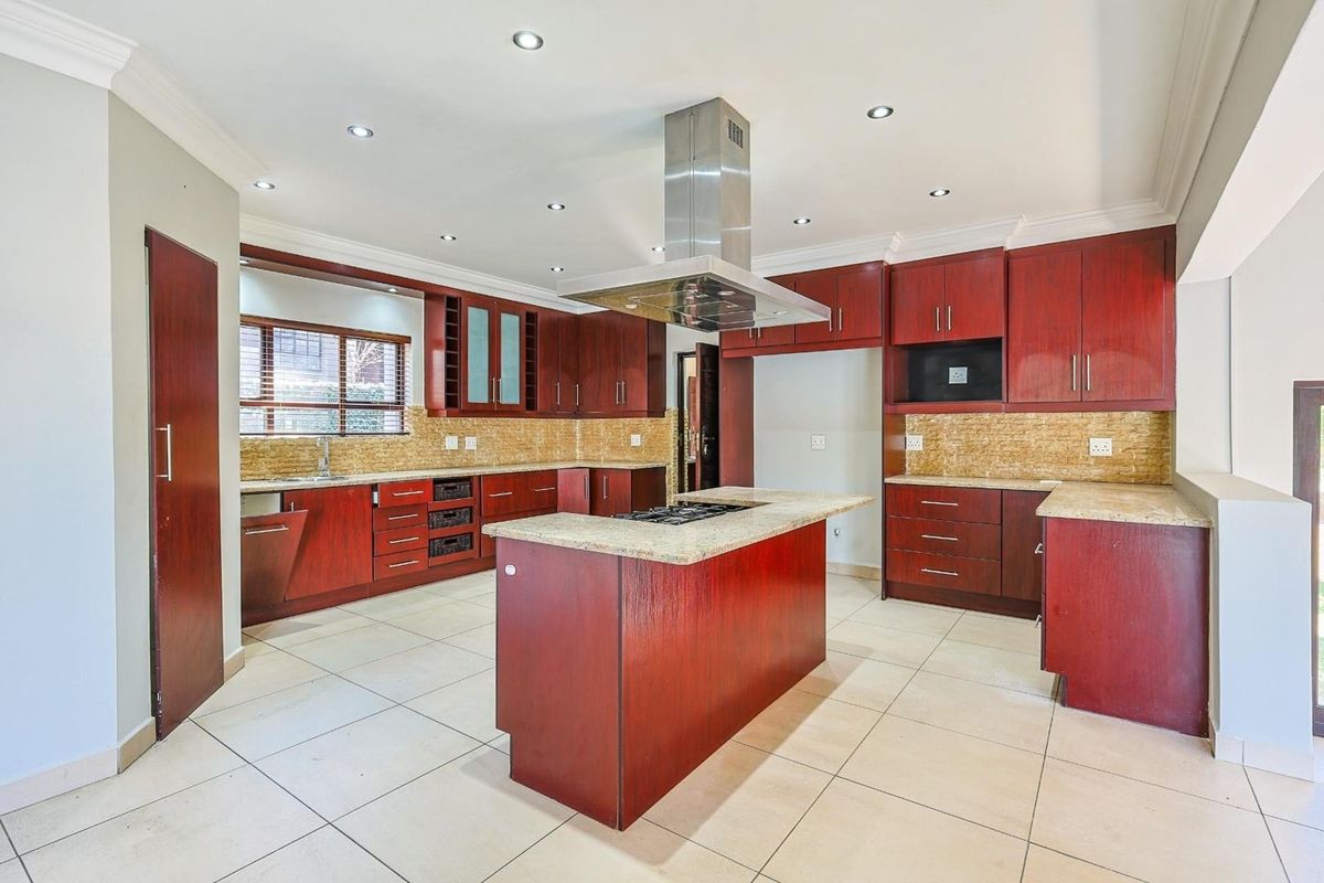 Spacious kitchen featuring dark wood cabinetry, stone countertops, a central island with a gas hob, and a stainless steel extractor fan.