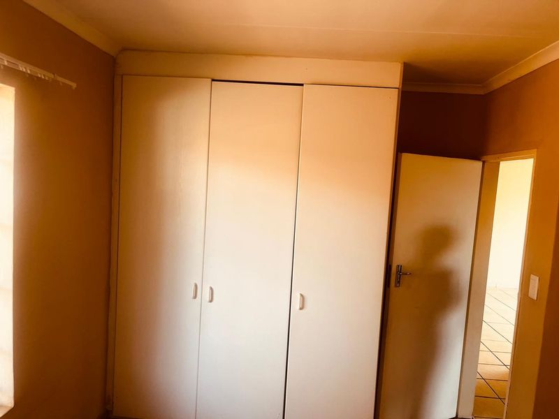 A simple bedroom featuring built-in cupboards, neutral wall finishes, and tiled flooring, offering a clean and functional space.